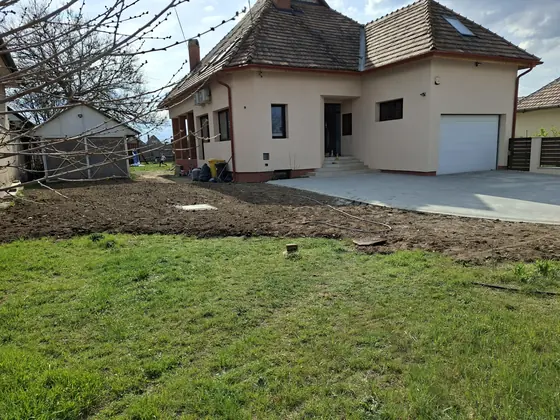 Betonozott kocsibeálló és rendezett kert a ház előtt