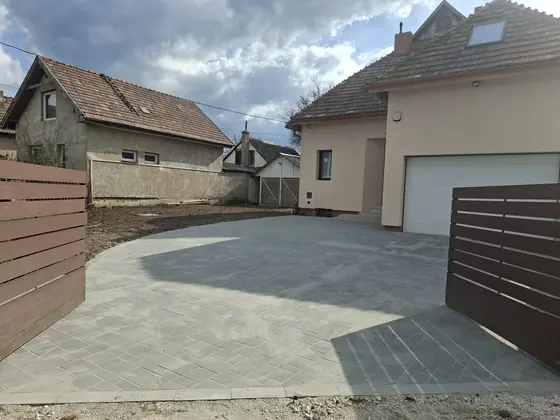 Térkövezett udvar fa kerítéssel és garázsbejáróval
